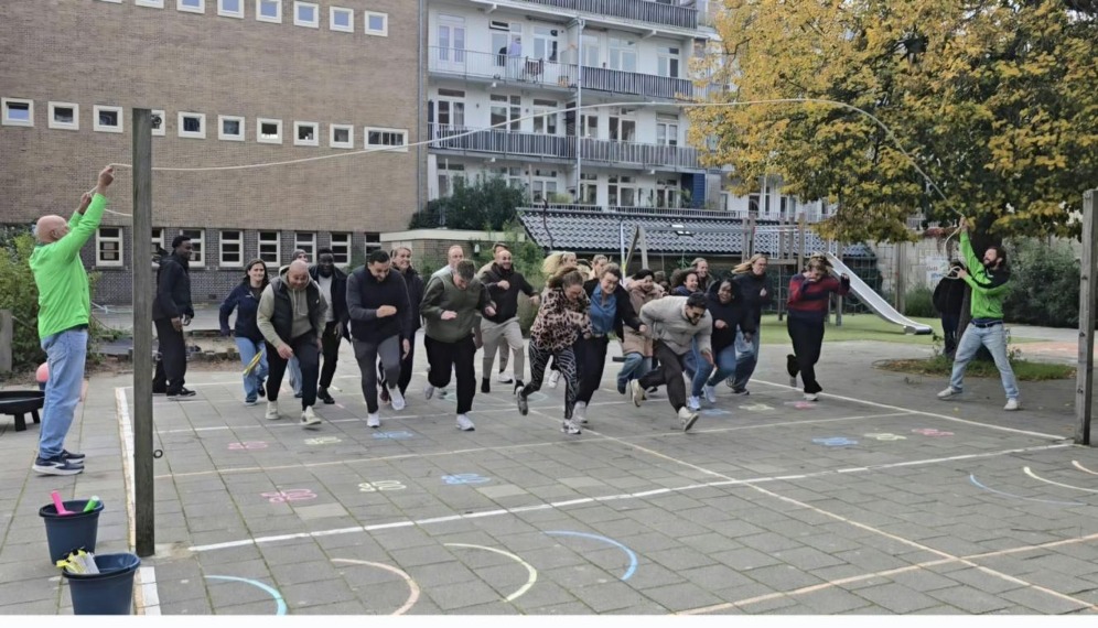 Een groep volwassenen rent lachend over een schoolplein tijdens een Beweeg Wijs-training